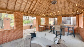 A covered patio area with a brick wall, a curved sofa, and a table with chairs.