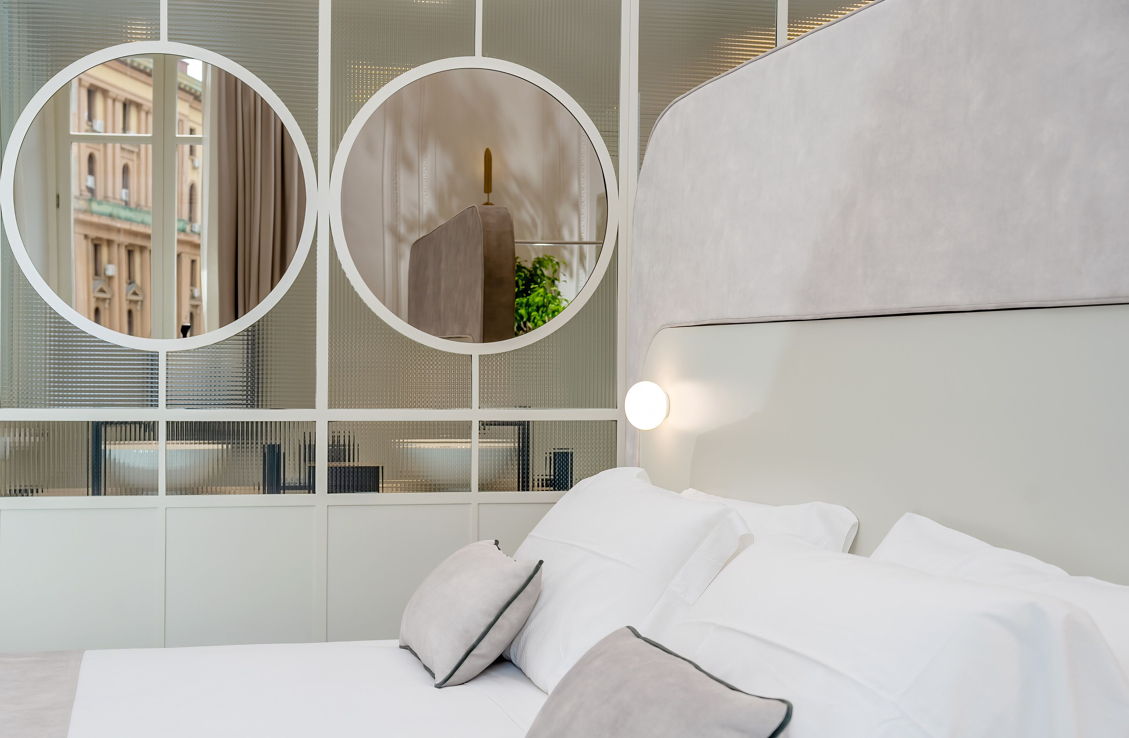 Una camera da letto moderna con un letto grande, due specchi rotondi e vista su un edificio attraverso una finestra.