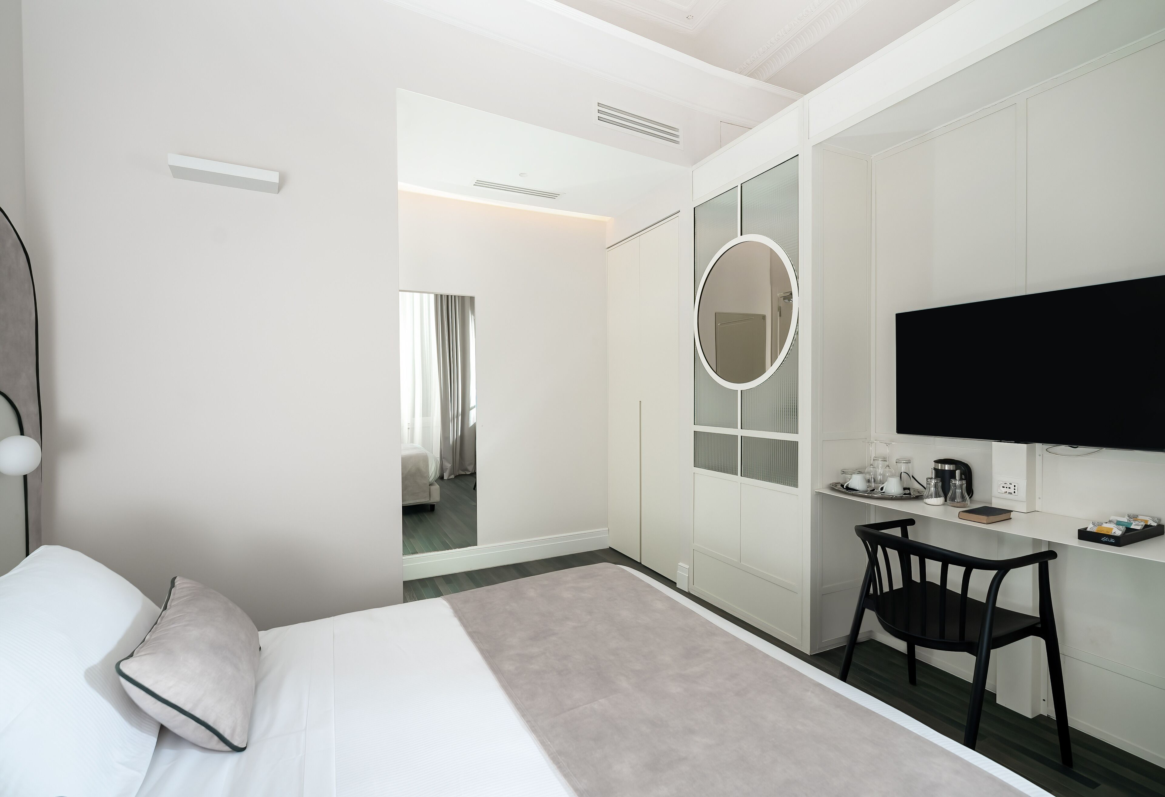 Moderni hotellihuone, jossa on sänky, työpöytä, tuoli, televisio ja peili.
