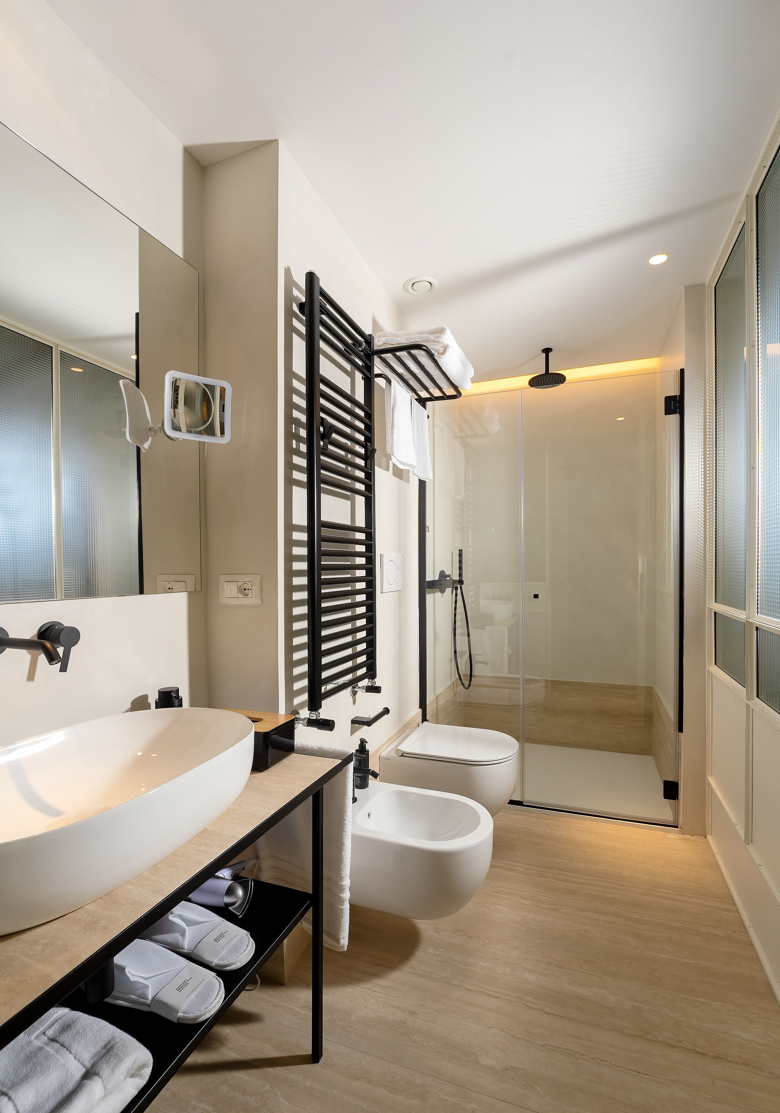 A modern bathroom with a large sink, two toilets, a shower enclosure, and a towel rack.