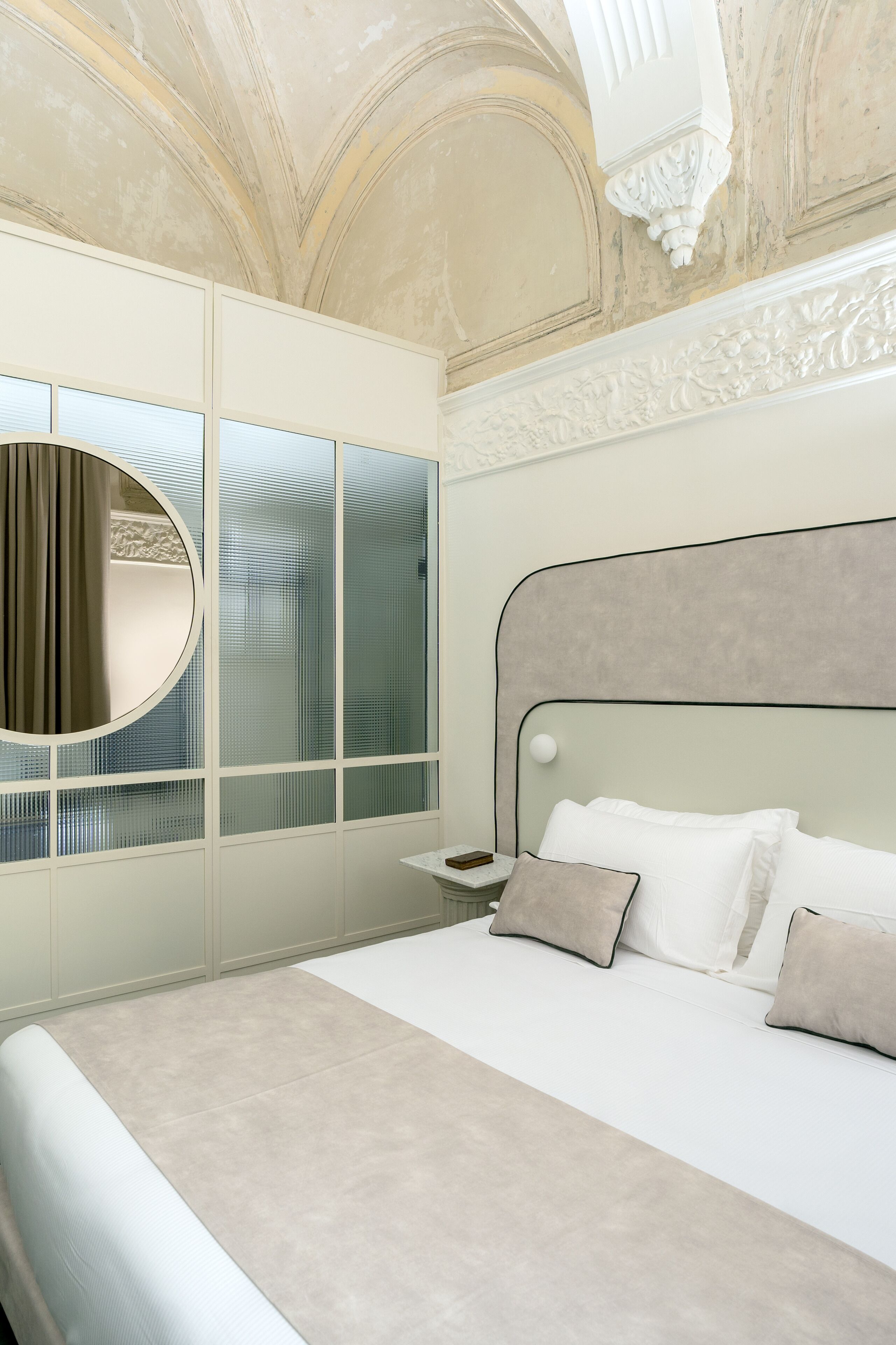 A bedroom with a large bed, a round mirror, and a window with curtains.