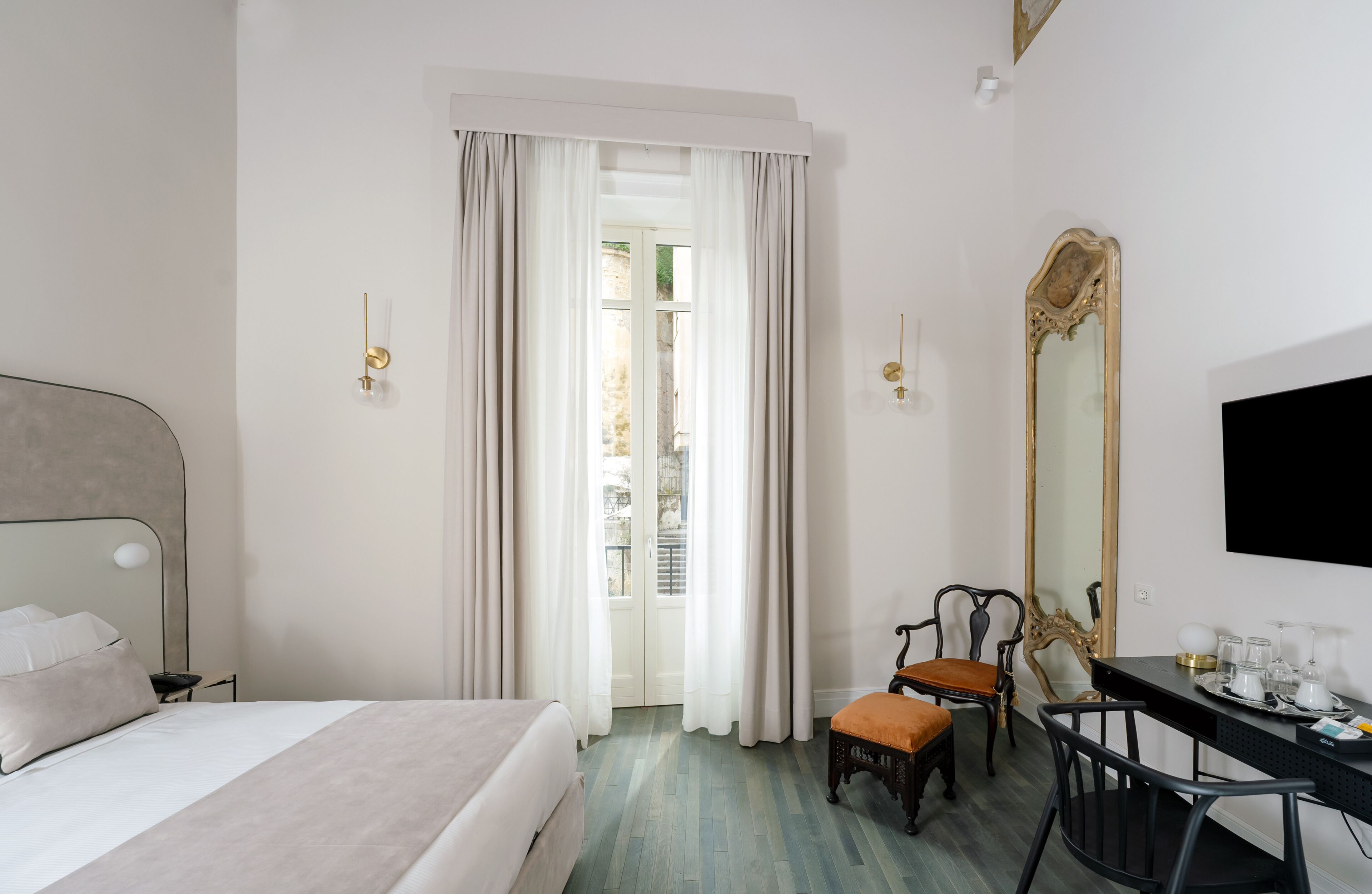 A hotel room with a bed, a desk, a chair, a large mirror, and a television.