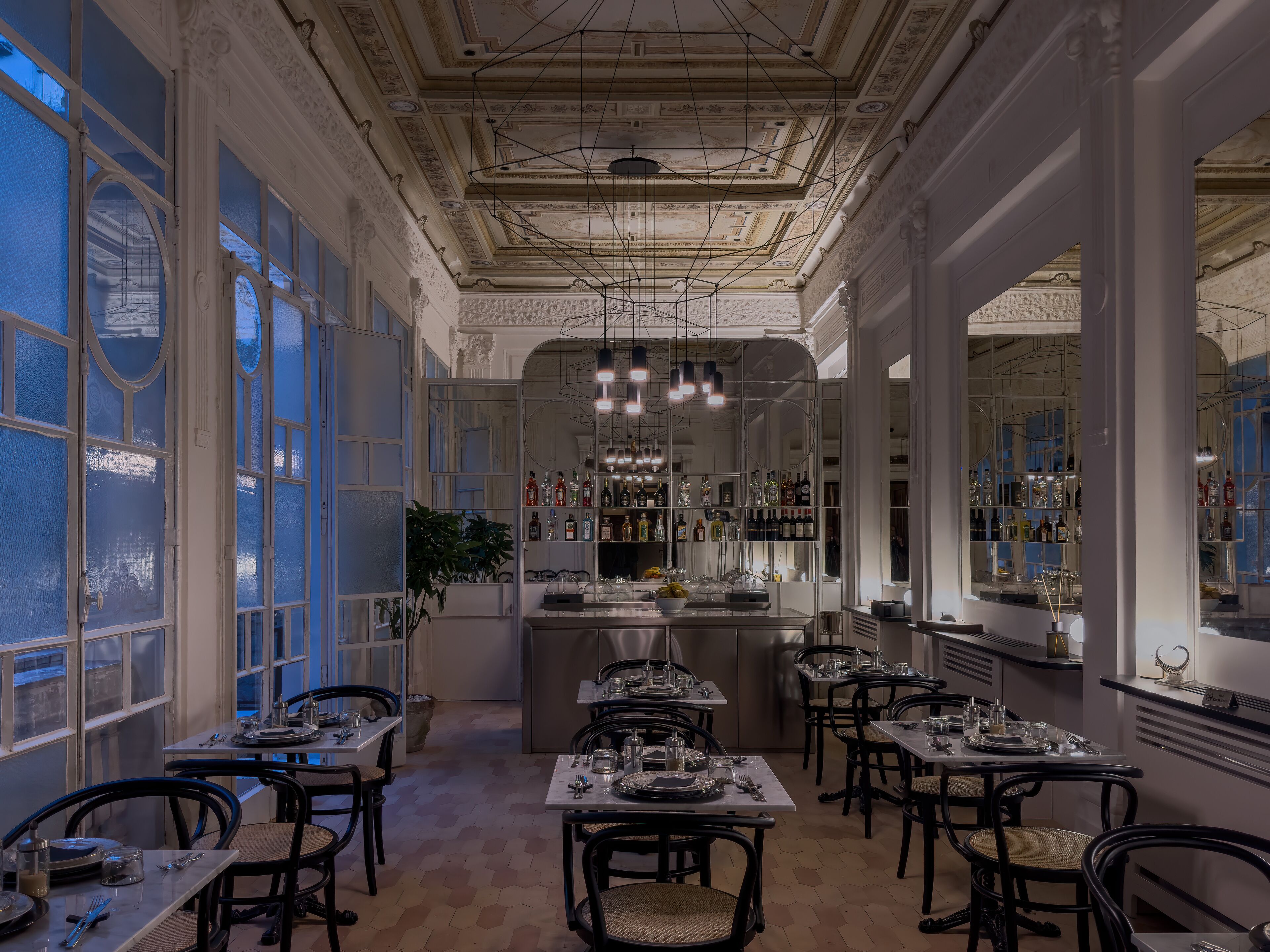 A restaurant with a classic interior, featuring a central bar, multiple dining tables, and a chandelier.