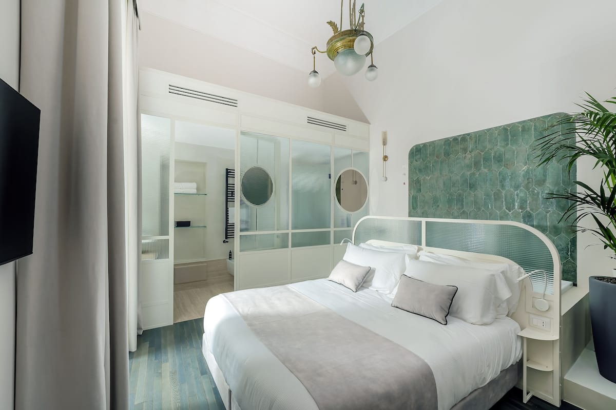 A modern bedroom with a large bed, a bedside table, a mirror, and a potted plant.