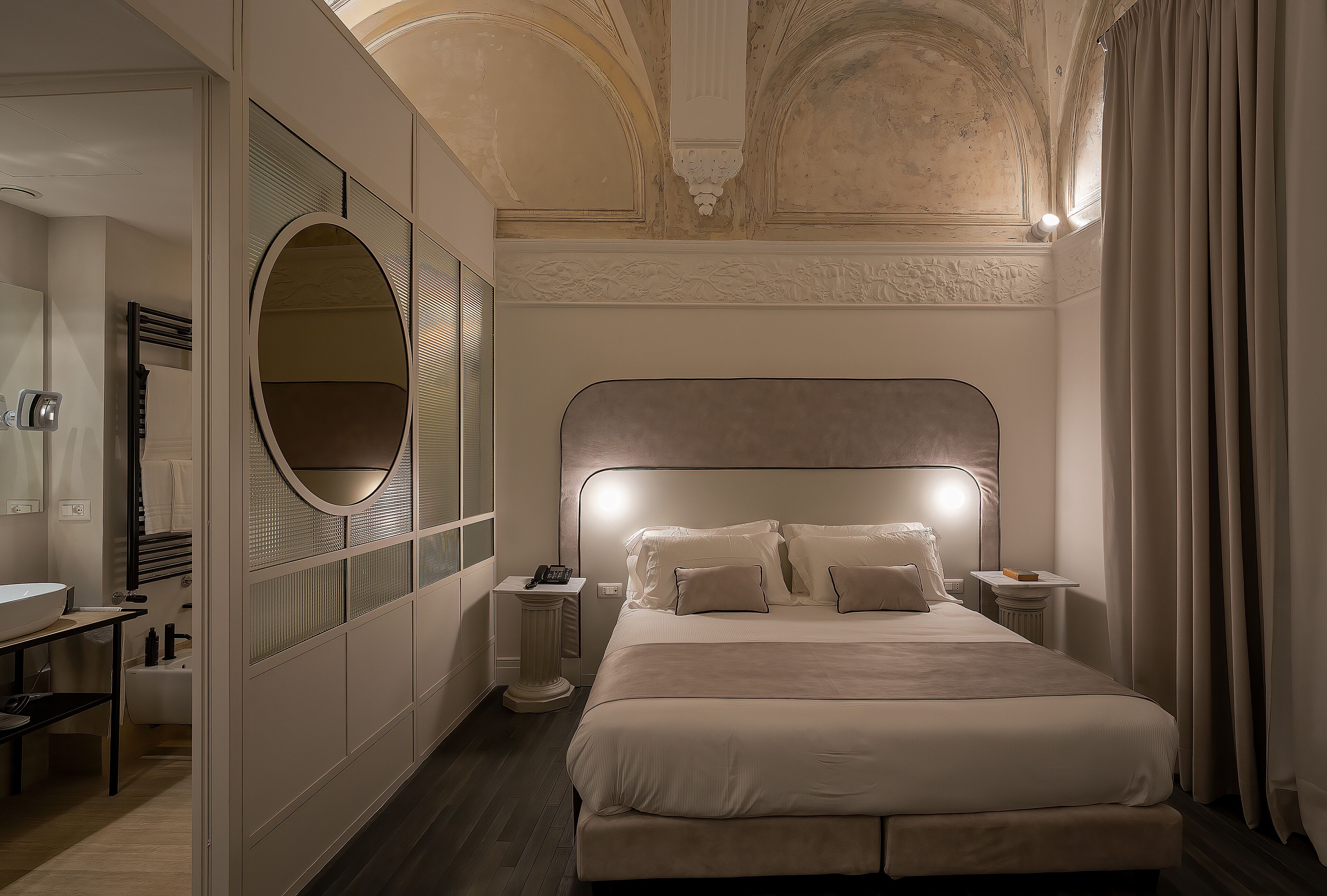 Ein modernes Hotelzimmer mit einem großen Bett, einem runden Spiegel, einem Nachttisch und einem Beistelltisch.