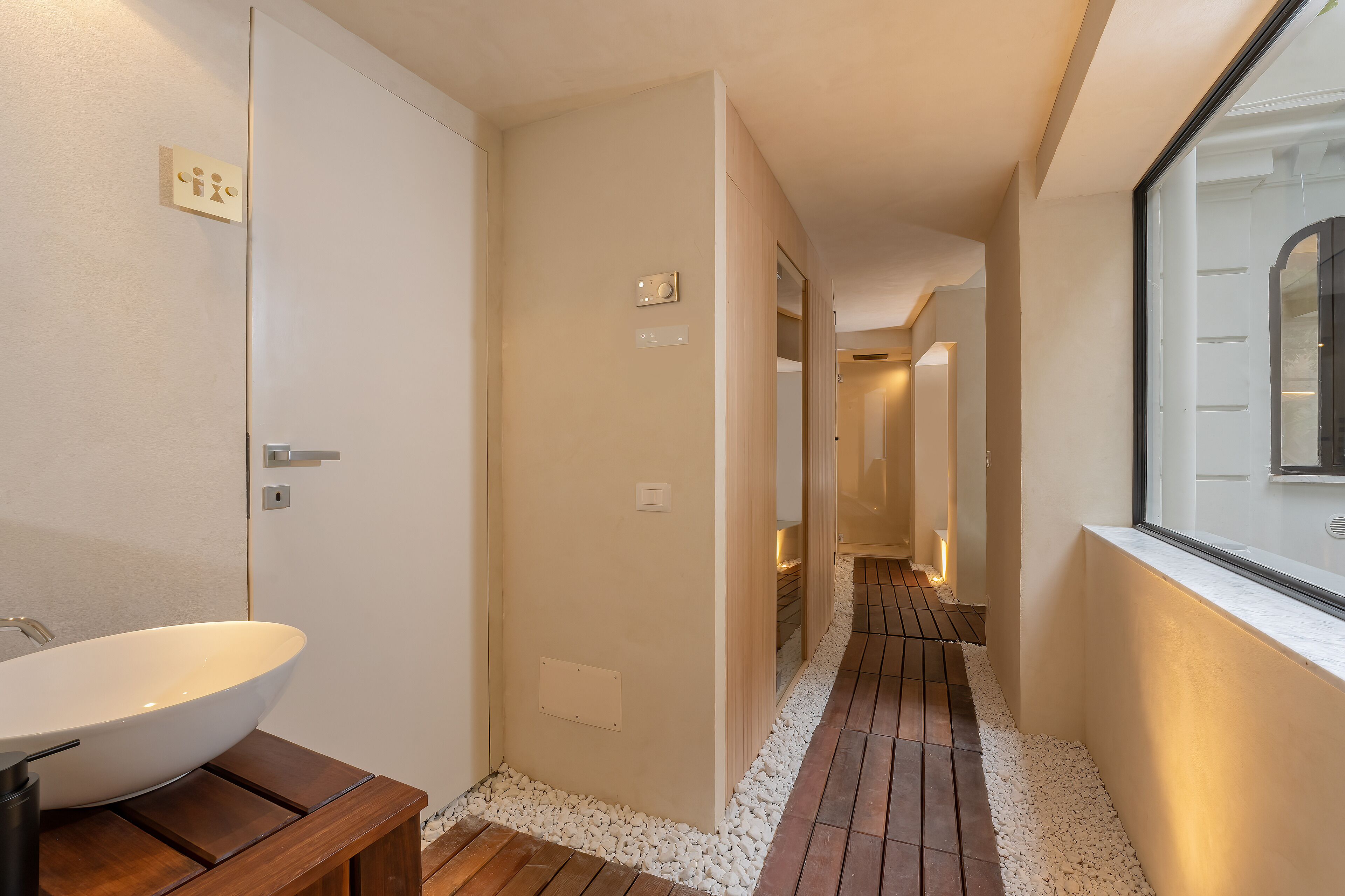 Een moderne badkamer met een groot wit wastafelblad, een houten bankje en een betegelde vloer.