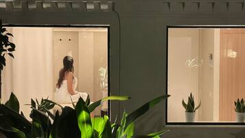 Een kamer met een groot raam, een bed en een spiegel. Planten staan op de voorgrond.