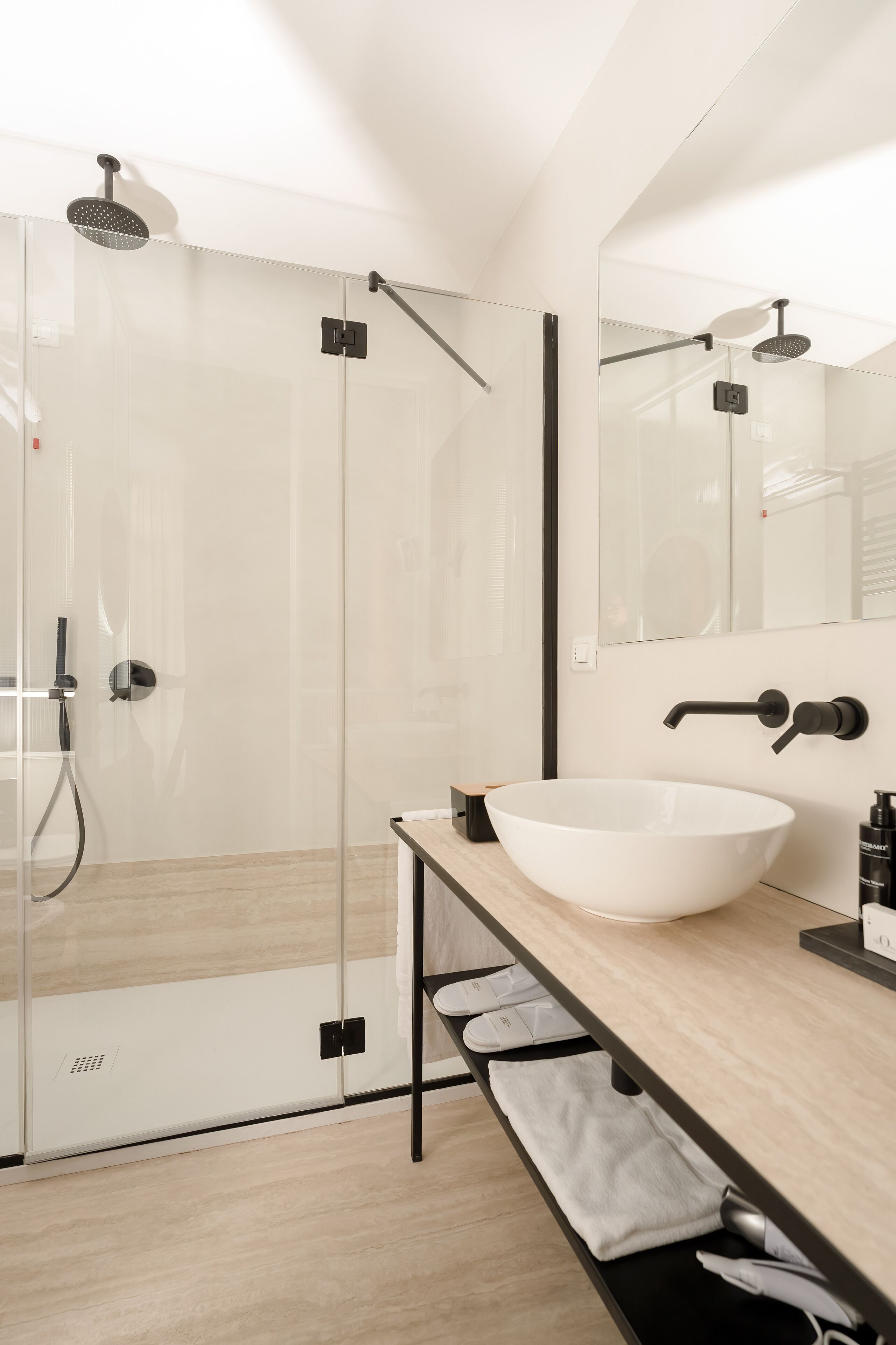 Een moderne badkamer met een glazen douchecabine, een witte wastafel en een spiegel erboven.