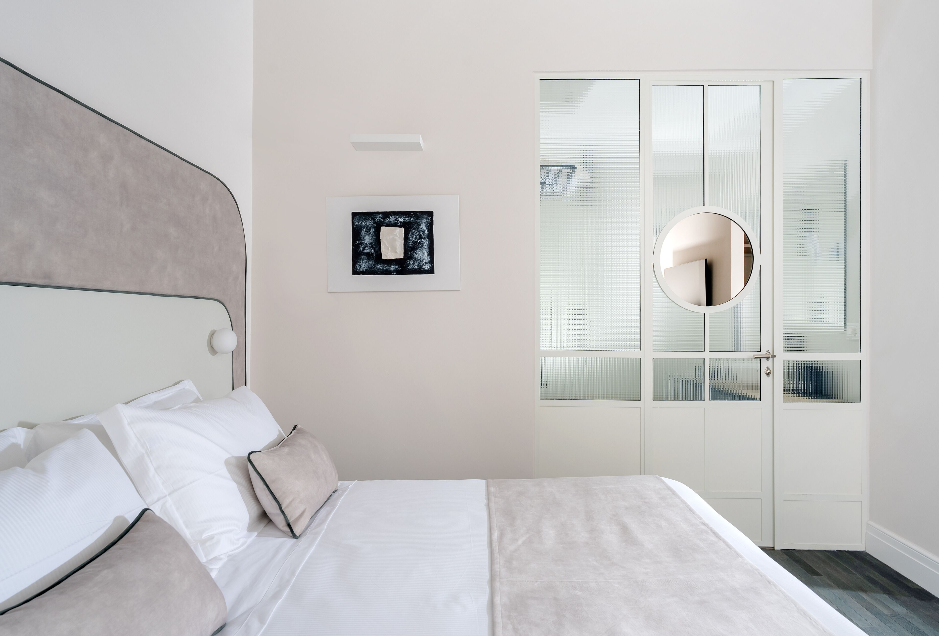 A neatly arranged bedroom with a bed, a bedside table, a wall-mounted mirror, and a framed picture.