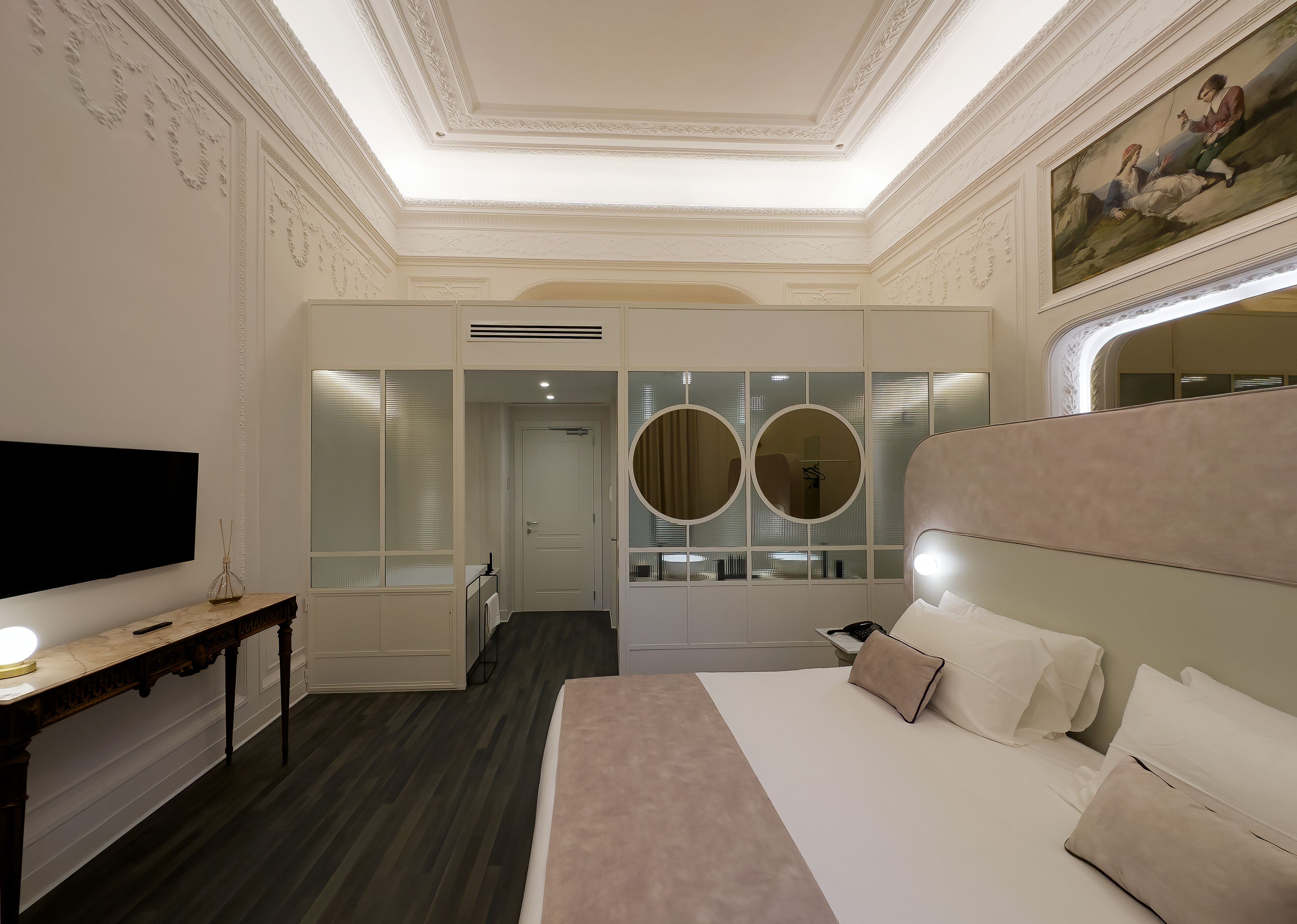 Una camera d'albergo con un letto grande, televisione, una toeletta con specchi e un soffitto con modanature elaborate.