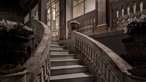 Una imponente escalera con escalones y barandillas de mármol, que conduce a un rellano con un amplio ventanal.