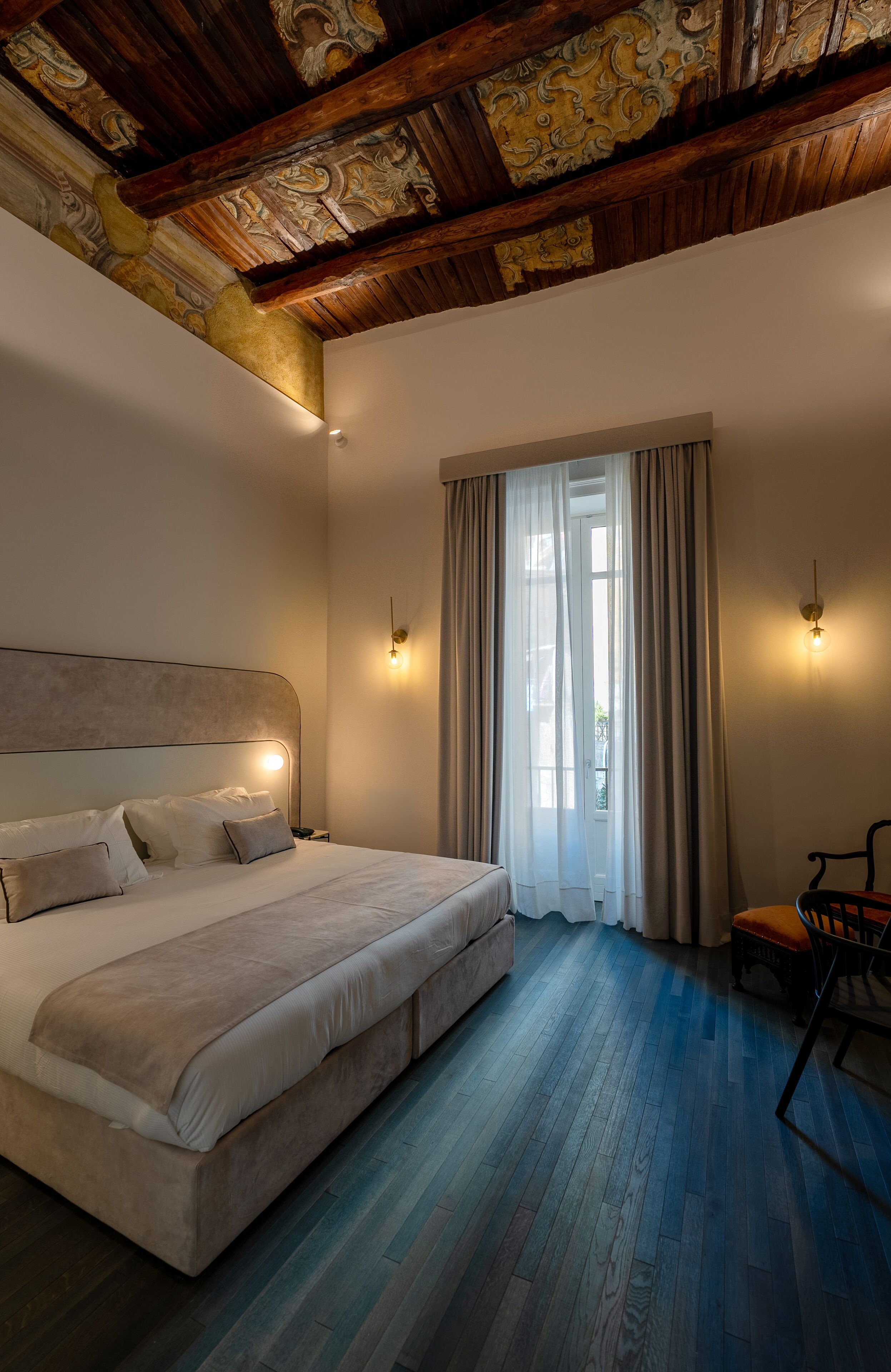Una camera da letto con un letto grande, soffitto in legno e vista all'aperto attraverso una finestra con tende.