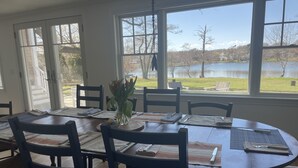 Zona pranzo con tavolo rotondo, sedie e vista su un lago attraverso ampie finestre.