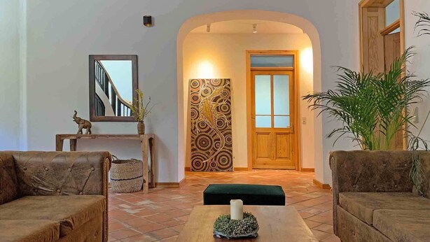 Ein gemütliches Wohnzimmer mit zwei Sofas, einem Couchtisch mit Kerze, einem Spiegel, einer Wand mit Muster und einer Holztür.