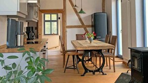 Eine moderne Küche mit Holzbalken, einem Esstisch mit Stühlen, einer Kaffeemaschine und einem großen Fenster.