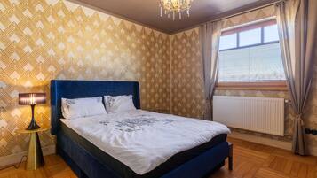A bedroom with a bed, a lamp, a window with curtains, and patterned wallpaper.