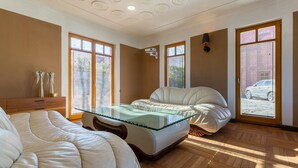 Un dormitorio con cama de cristal, suelo de madera y ventanas grandes con persianas.