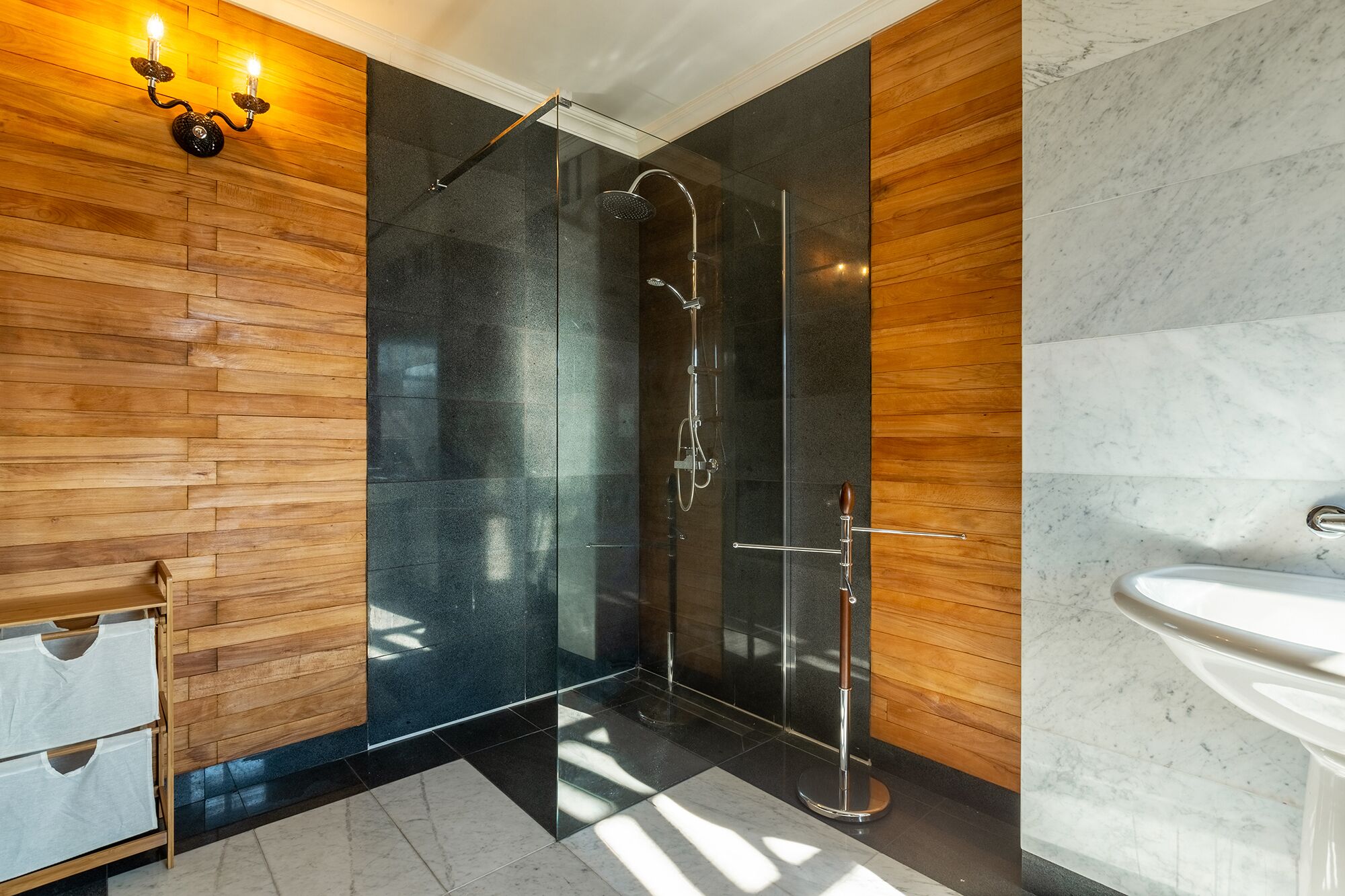 A modern bathroom with a glass-enclosed shower, wooden wall panels, and a marble countertop.