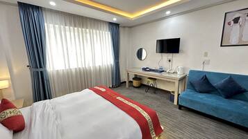 Una habitación de hotel con cama, escritorio, sofá azul, televisor y ventana con cortinas.