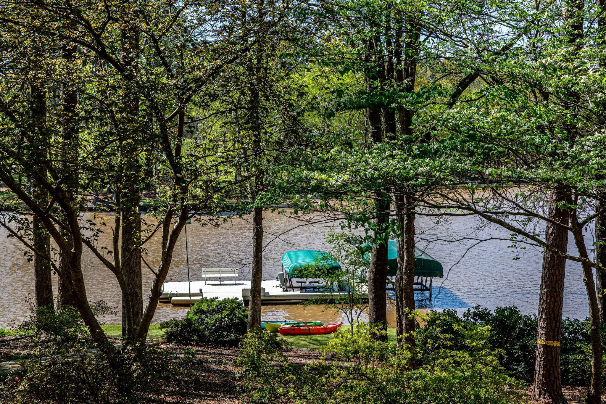 A lakeside view with a dock, a covered boat, and a canoe.