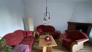 Ein Wohnzimmer mit rotem Sofagarnitur, einem Holztisch und einem Kamin.