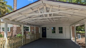 Een overdekt buitengebied met een bakstenen gebouw, een houten hek en een zwarte deur.