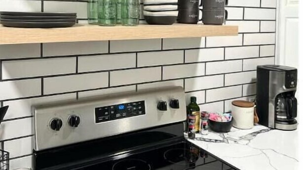 Een keuken met een modern design, met een roestvrijstalen fornuis, een zwart-wit betegelde spatwand en houten planken met verschillende keukenbenodigdheden.
