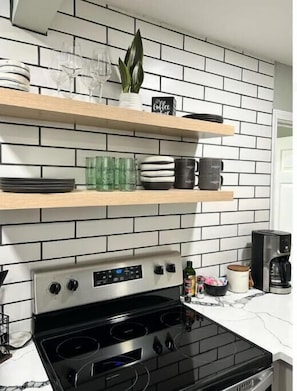 Una cocina de diseño moderno, con estufa de acero inoxidable, salpicadero de azulejos blanco y negro y estantes de madera con diversos utensilios de cocina.