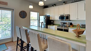 A modern kitchen with white cabinets, a central island, bar stools, a refrigerator, a microwave, and a stove. - Bonita Point Condo II #214E by Resort Collection (Panama City Beach)