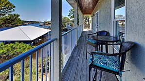A covered outdoor area with a wooden deck, a table with chairs, and a view of the water and buildings in the background. - Bonita Point Condo II #214E by Resort Collection (Panama City Beach)