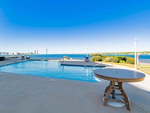 A swimming pool with a view of the sea, a wooden table, and a lamp post.