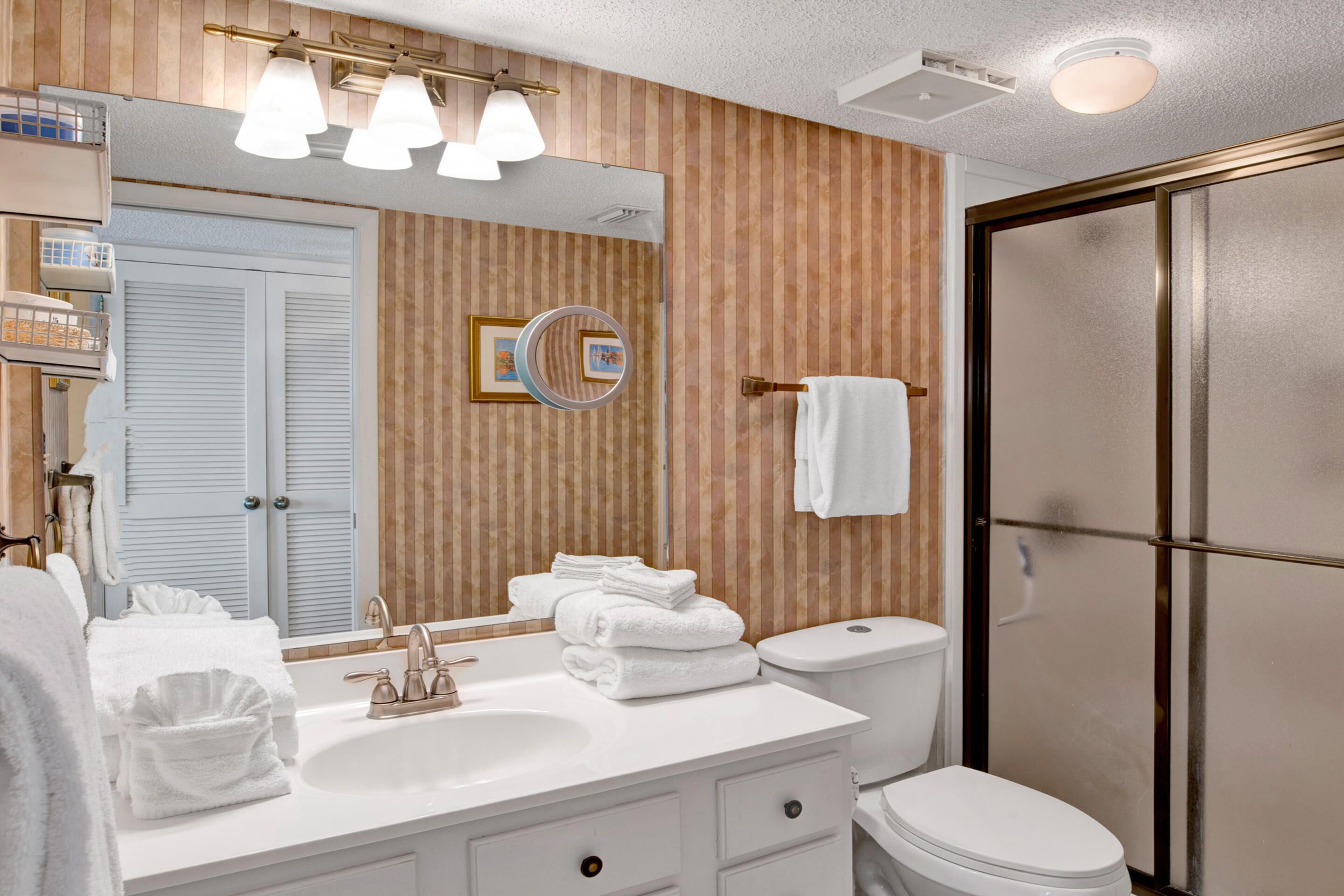 Een moderne badkamer met een wastafel, wasbak en spiegel. Er is een toilet en een douchecel te zien.