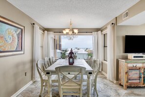 A dining area with a table and chairs, a chandelier, a television, and a view of the ocean.