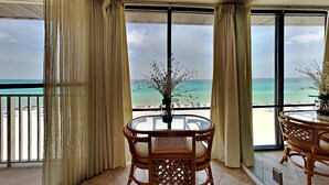 Een balkon met uitzicht op het strand, een ronde tafel met stoelen en een vaas met bloemen.