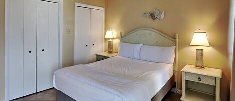A bedroom with a bed, two bedside tables with lamps, a nightstand, a decorative wall piece, and two wardrobes.