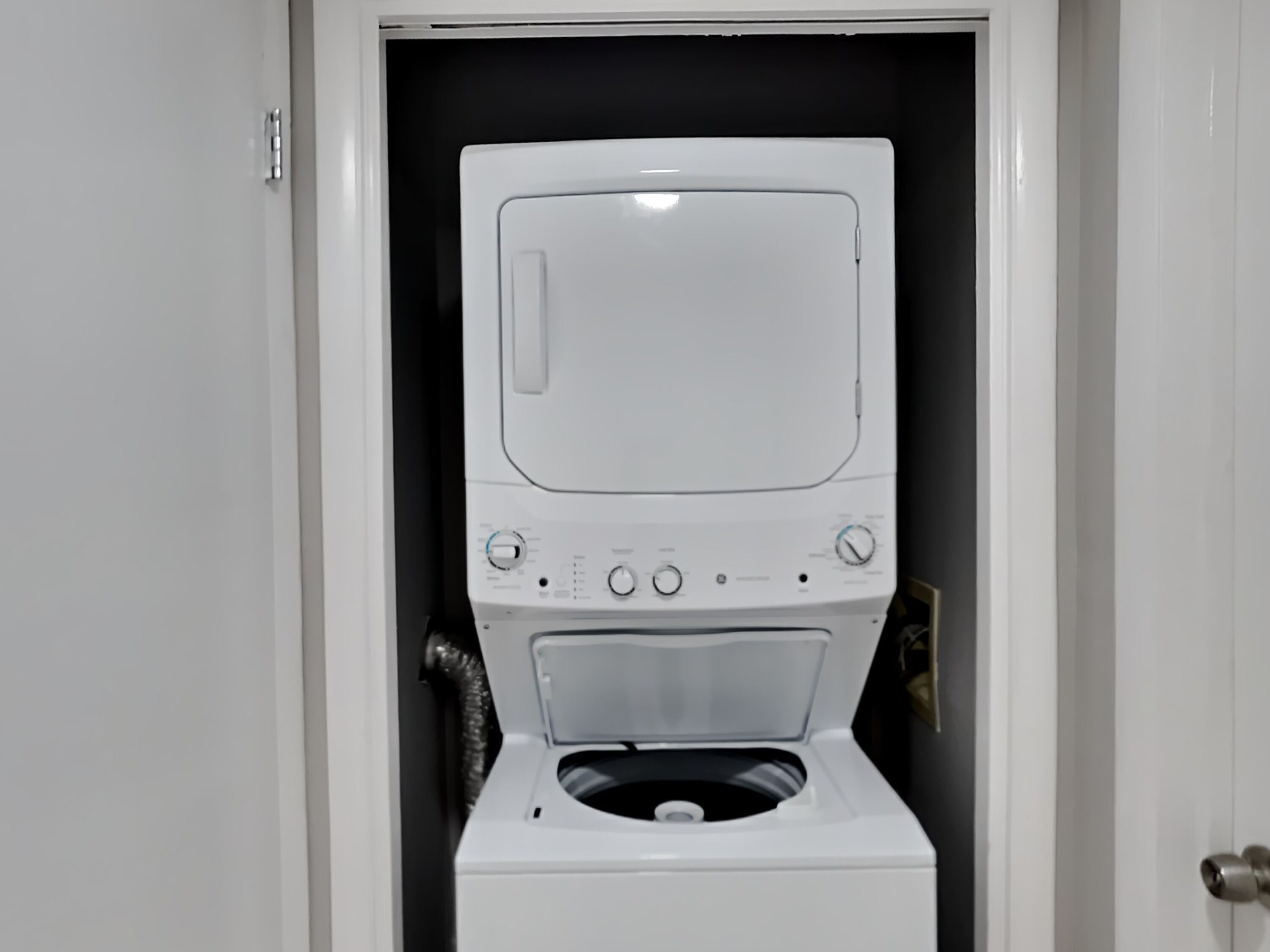 A front view of a white washing machine in a laundry room with a black wall and a white door.