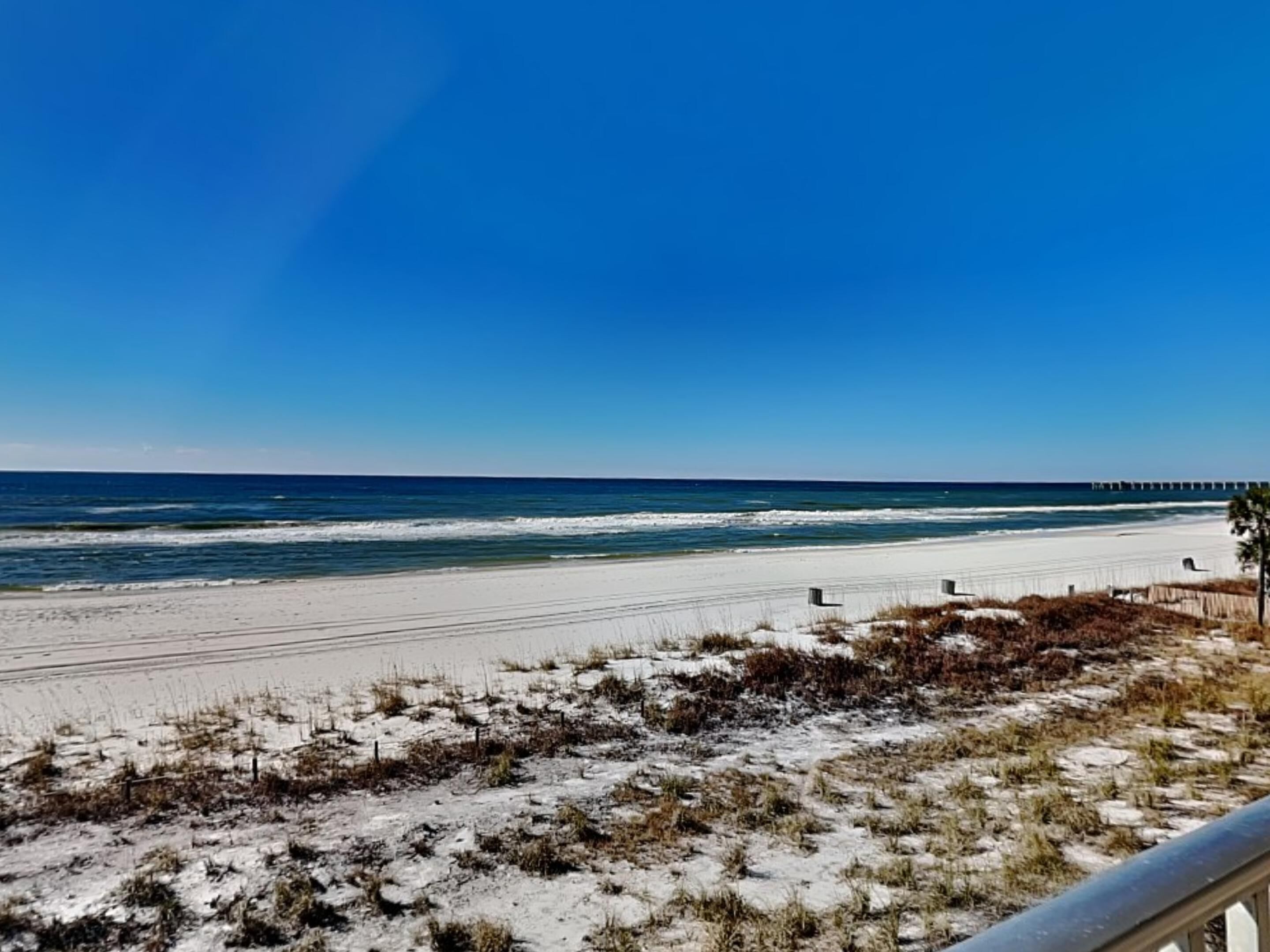 A beach with a clear sky, sandy shore, and a pier in the distance.
