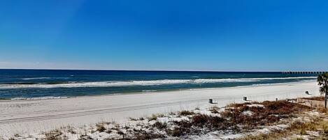 A beach with a clear sky, sandy shore, and a pier in the distance.