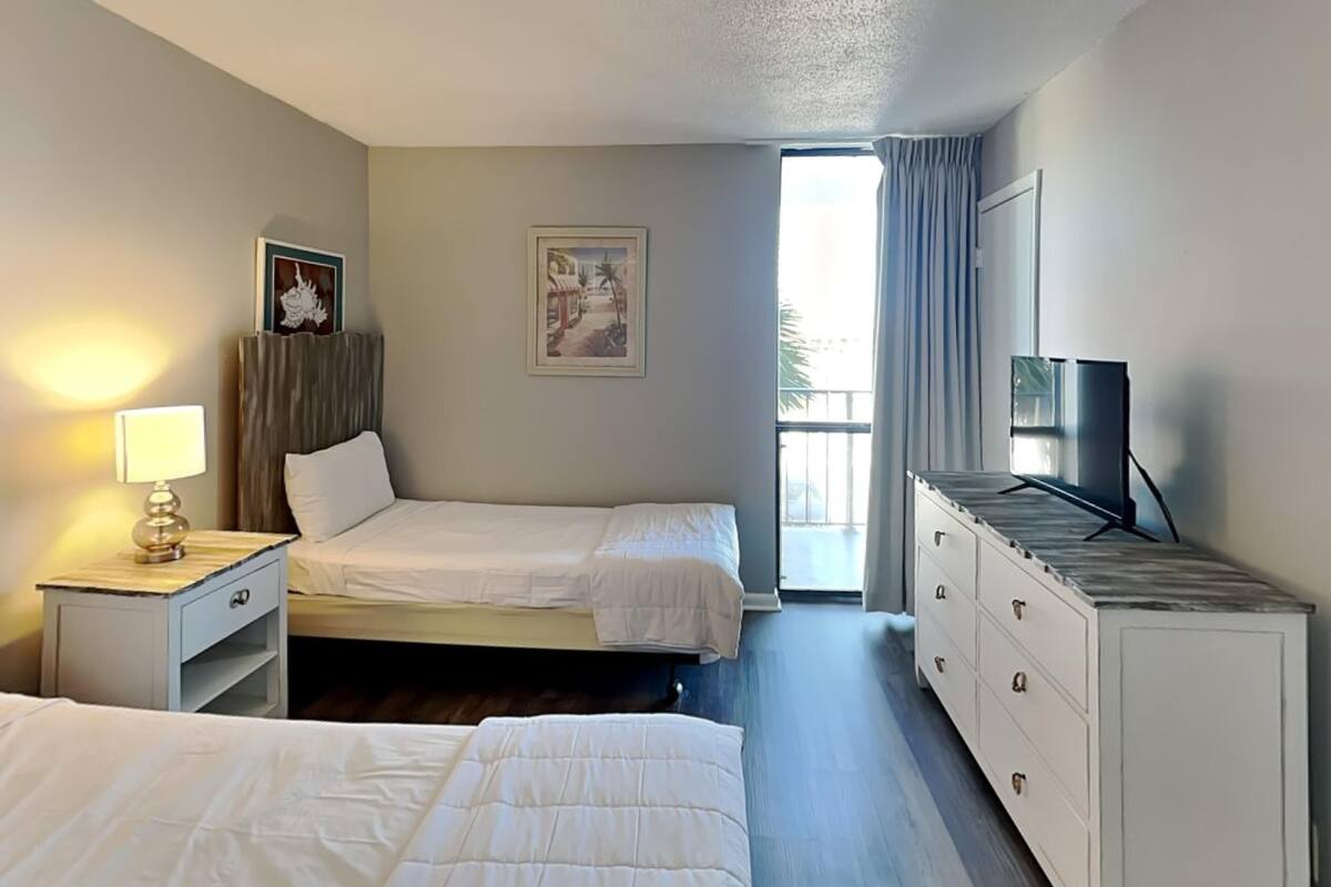 Una camera d'albergo con due letti, una televisione, una cassettiera e un quadro appeso al muro.