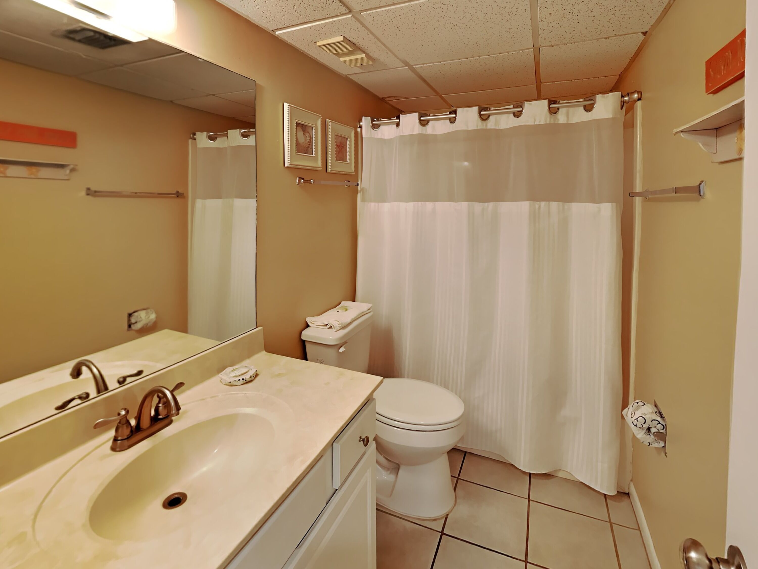 Un baño con lavamanos, espejo, inodoro y cortina de ducha.