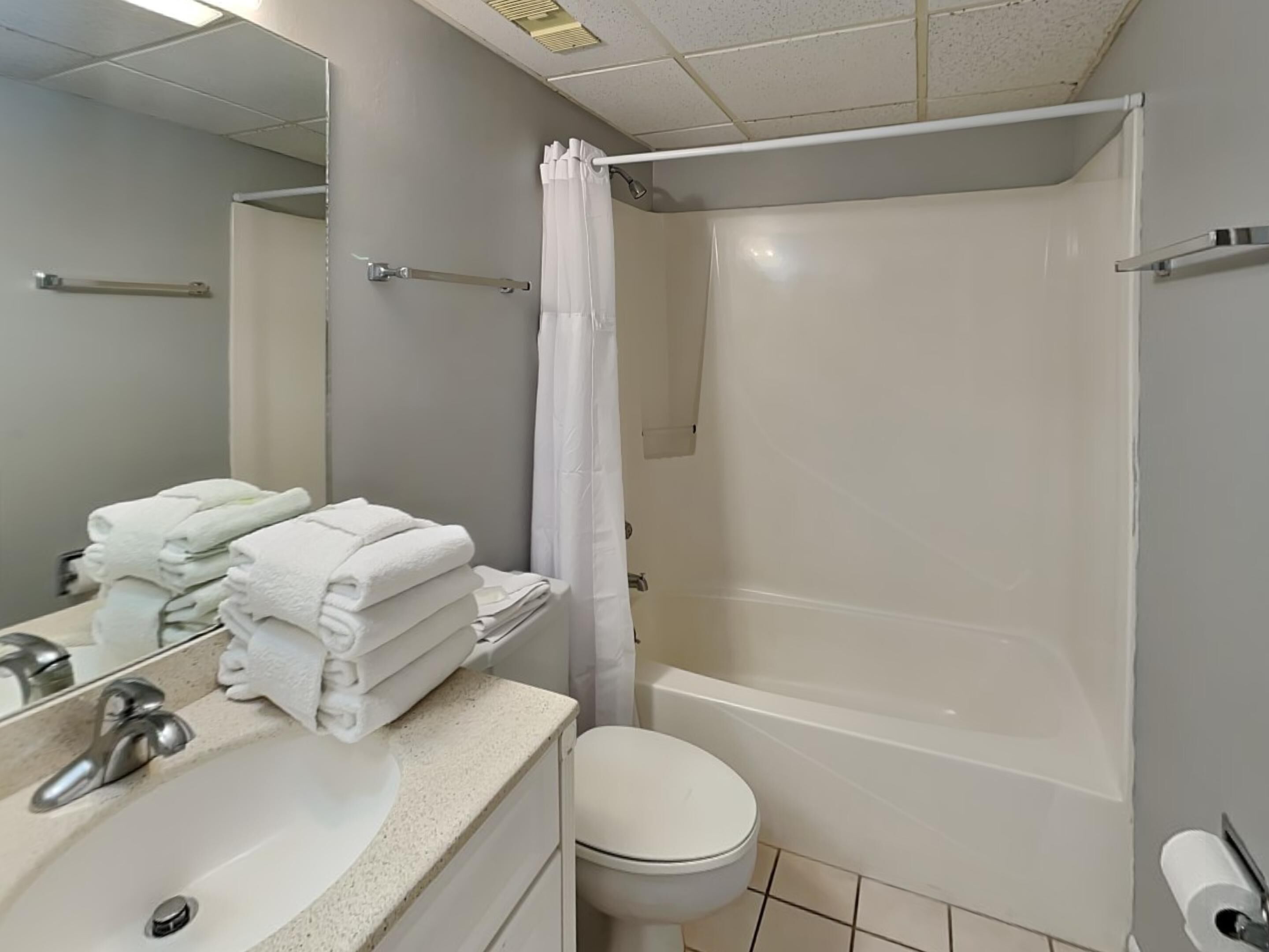 A bathroom with a sink, toilet, and bathtub. There are towels stacked on the sink.