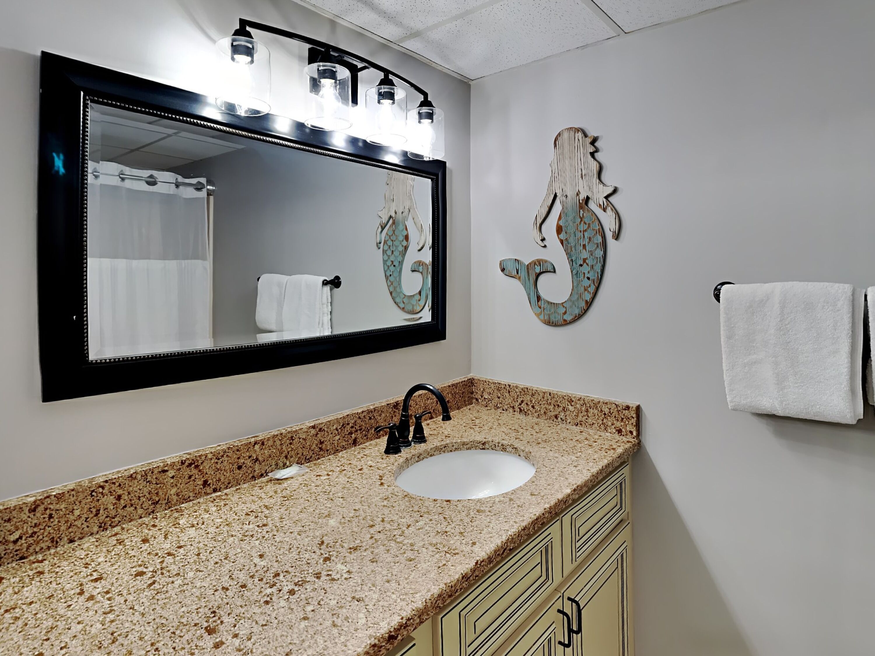 Une salle de bain avec un comptoir en granit, un lavabo, un miroir et un porte-serviettes.