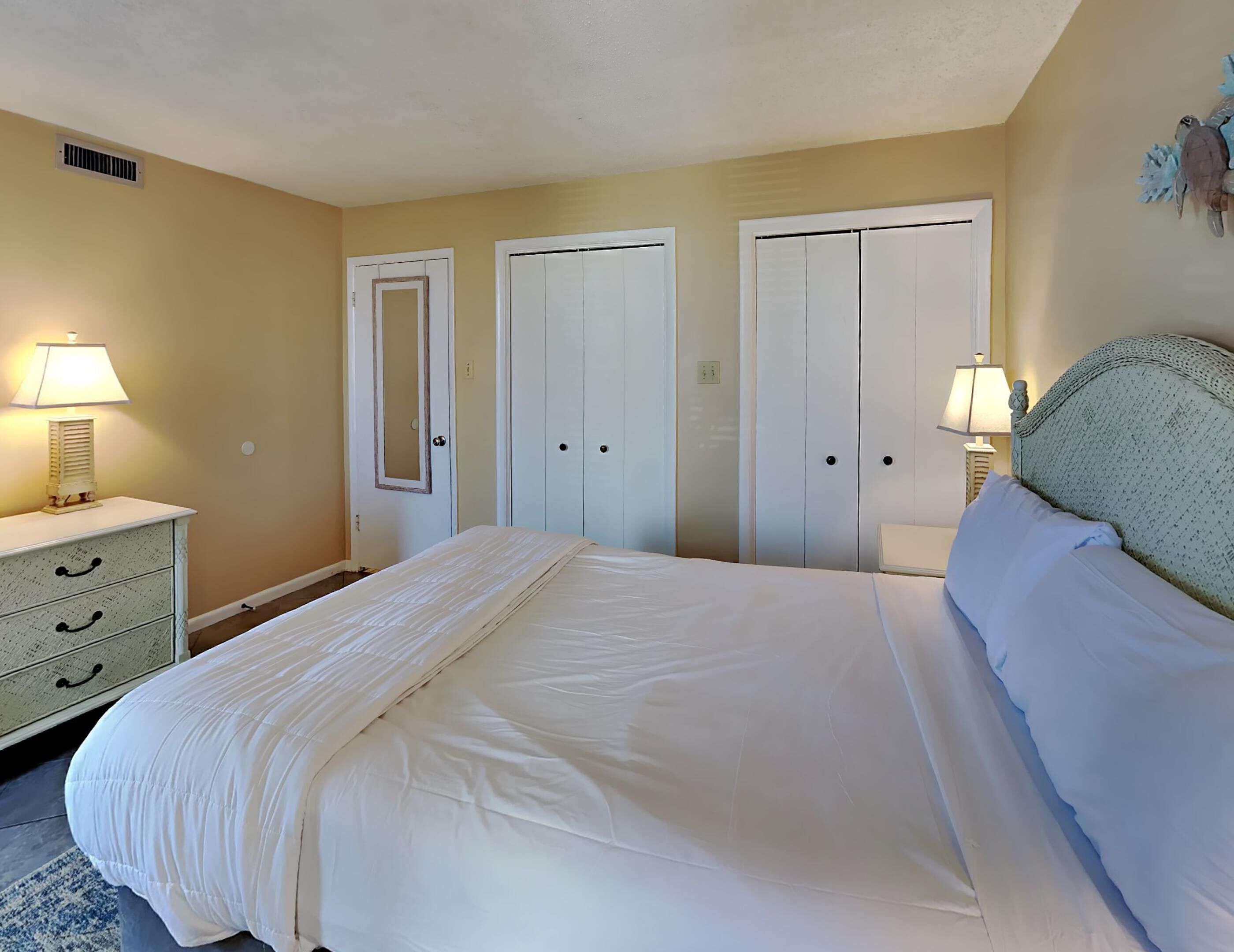 Um quarto com uma cama, duas mesas de cabeceira com luminárias, um penteadeira e um guarda-roupa.