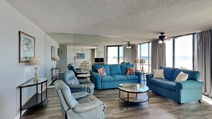 Een ruime woonkamer met een blauwe bank, een lederen fauteuil en een salontafel. Op de achtergrond is een eethoek met een tafel en stoelen te zien.