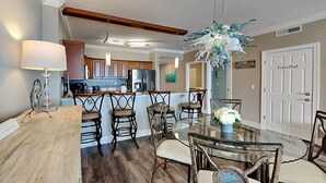 Uma área de refeições com mesa de vidro e cadeiras, piso de madeira e luminária decorativa no teto.