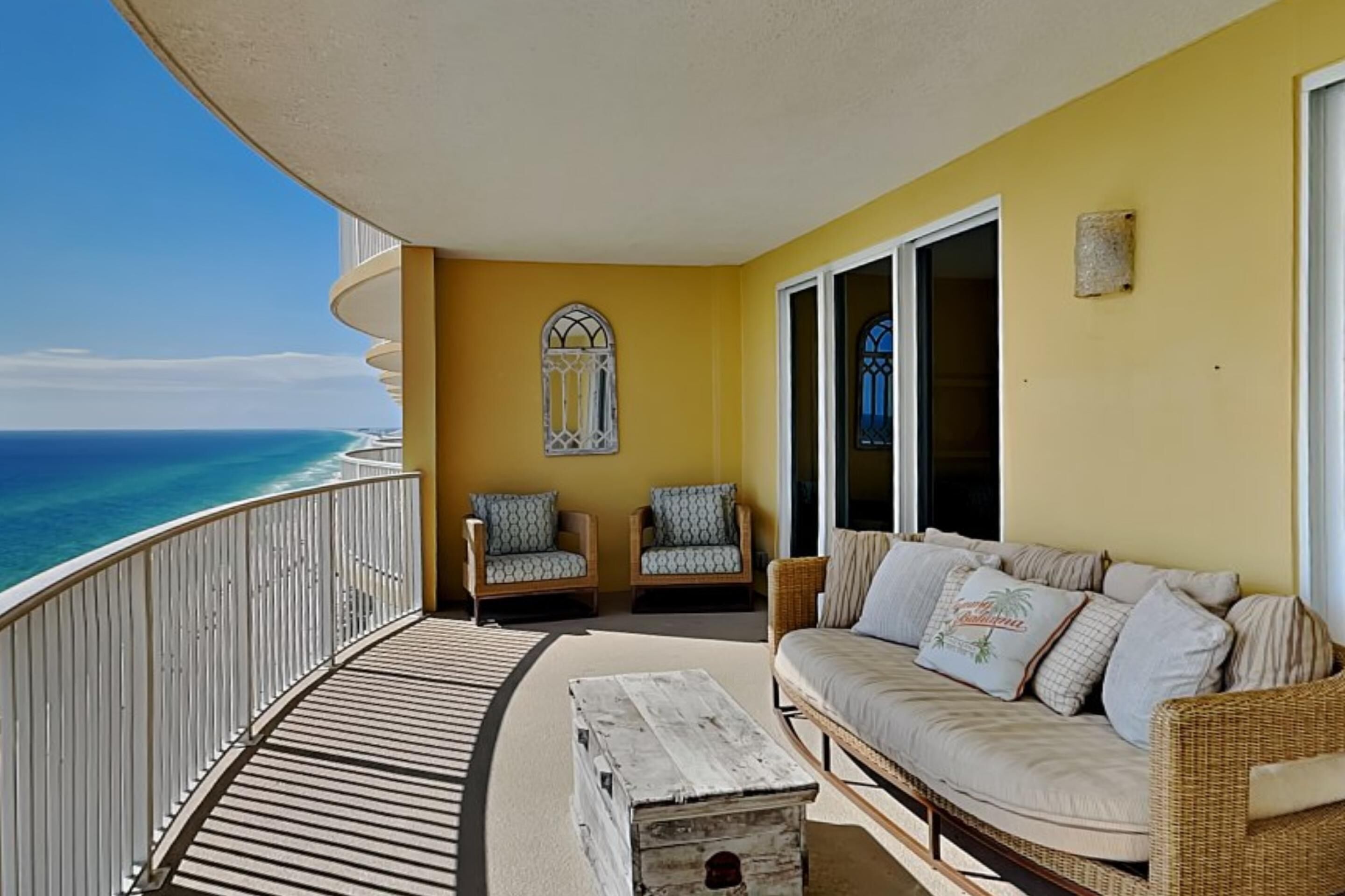A balcony with a view of the ocean, wicker furniture, and a wooden table.