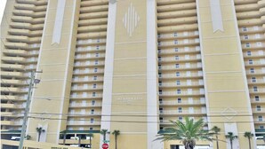 Um hotel de vários andares com fachada amarela, varandas em cada andar e um emblema bem visível no centro.