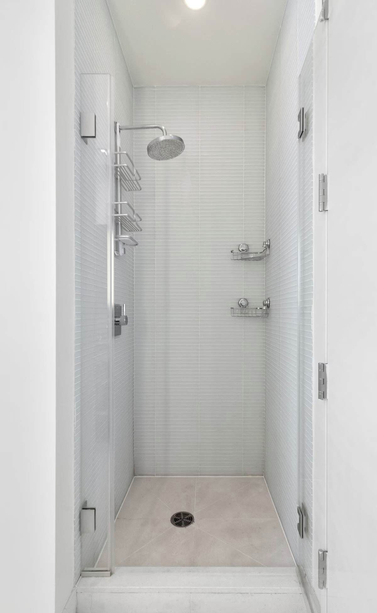 A modern shower stall with a glass door, a handheld showerhead, and a floor drain.