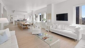 Un salon moderne et bien éclairé, avec un canapé blanc, une table basse en verre et un coin repas comprenant une table et des chaises blanches.