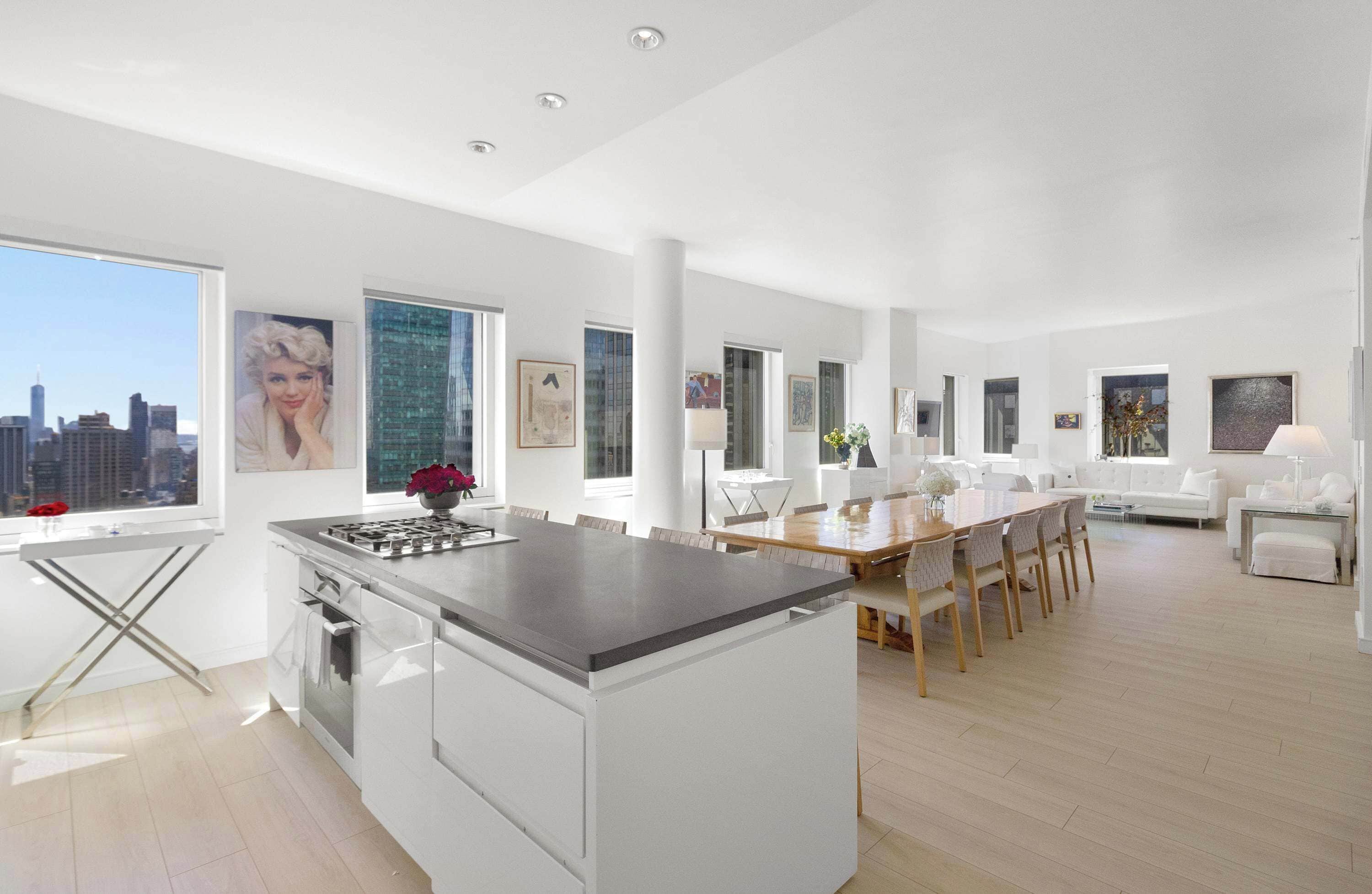 A modern kitchen with a central island, dining area with a wooden table and chairs, and a living room with a white sofa and a coffee table.